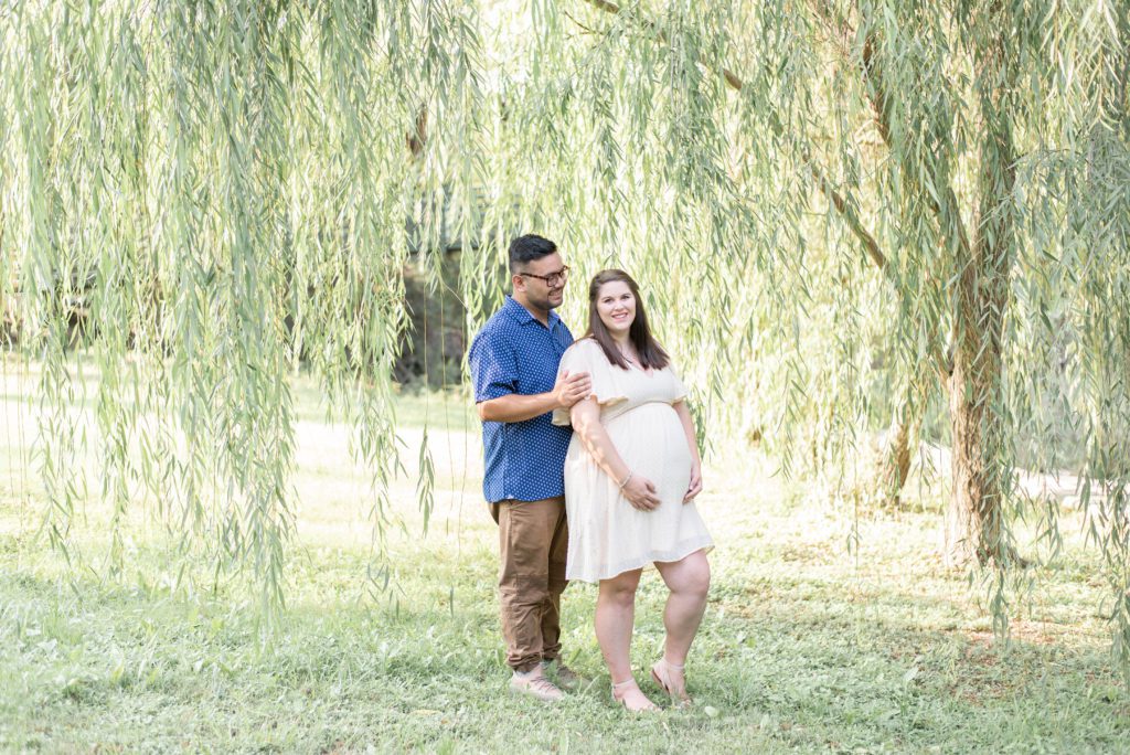 man lovingly smiles at his pregnant wife under a willow tree at airfield falls in fort worth