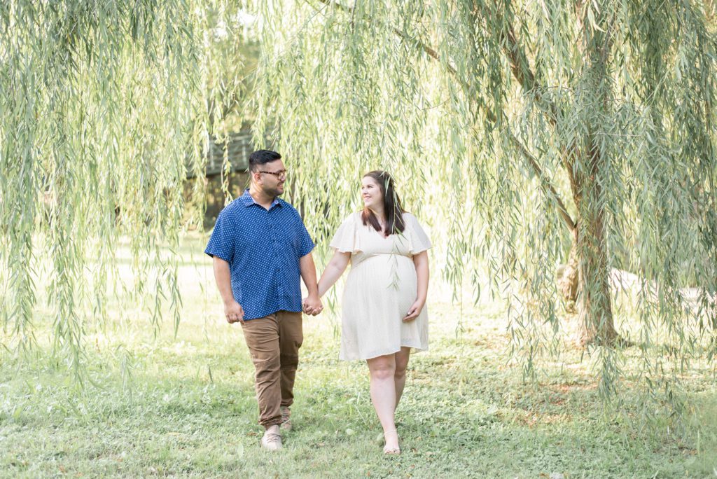 expecting couple walk hand in hand under a willow tree at airfield falls in fort worth