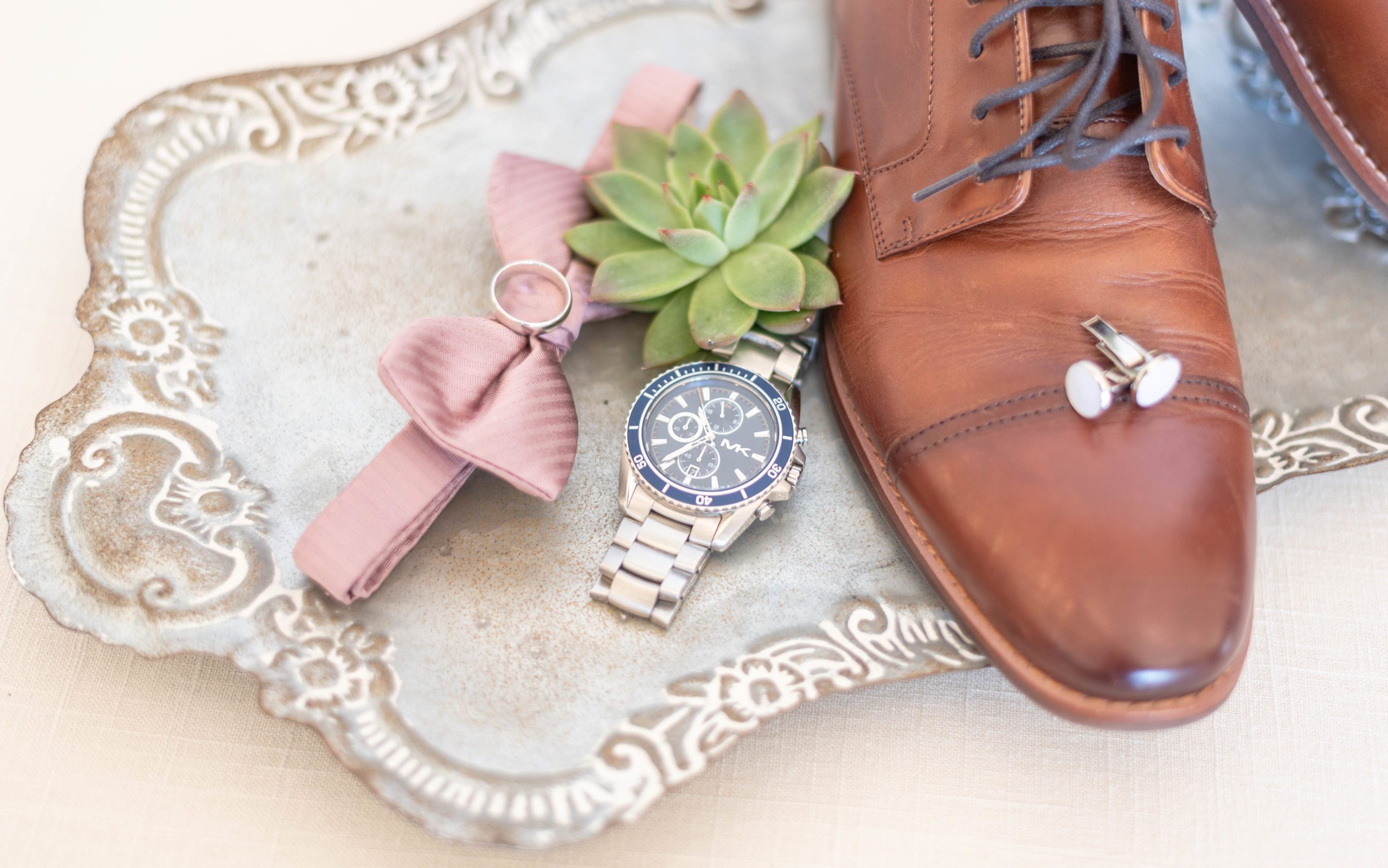 Groom wedding details such as shoes, watch and bow tie styled on a vintage tray