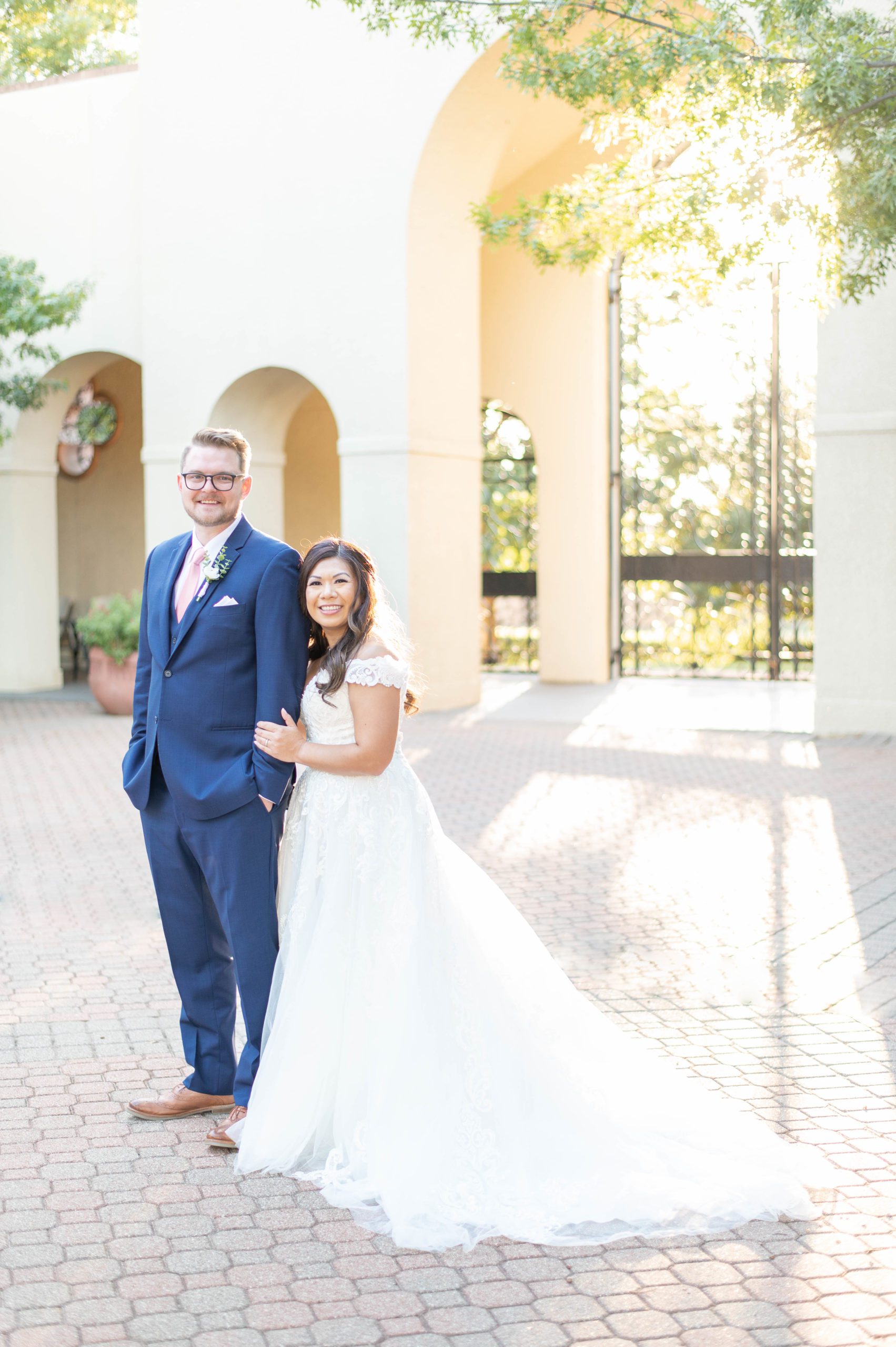 bride and groom smile at camera in a beautifully lit church courtyard at their modern romantic wedding