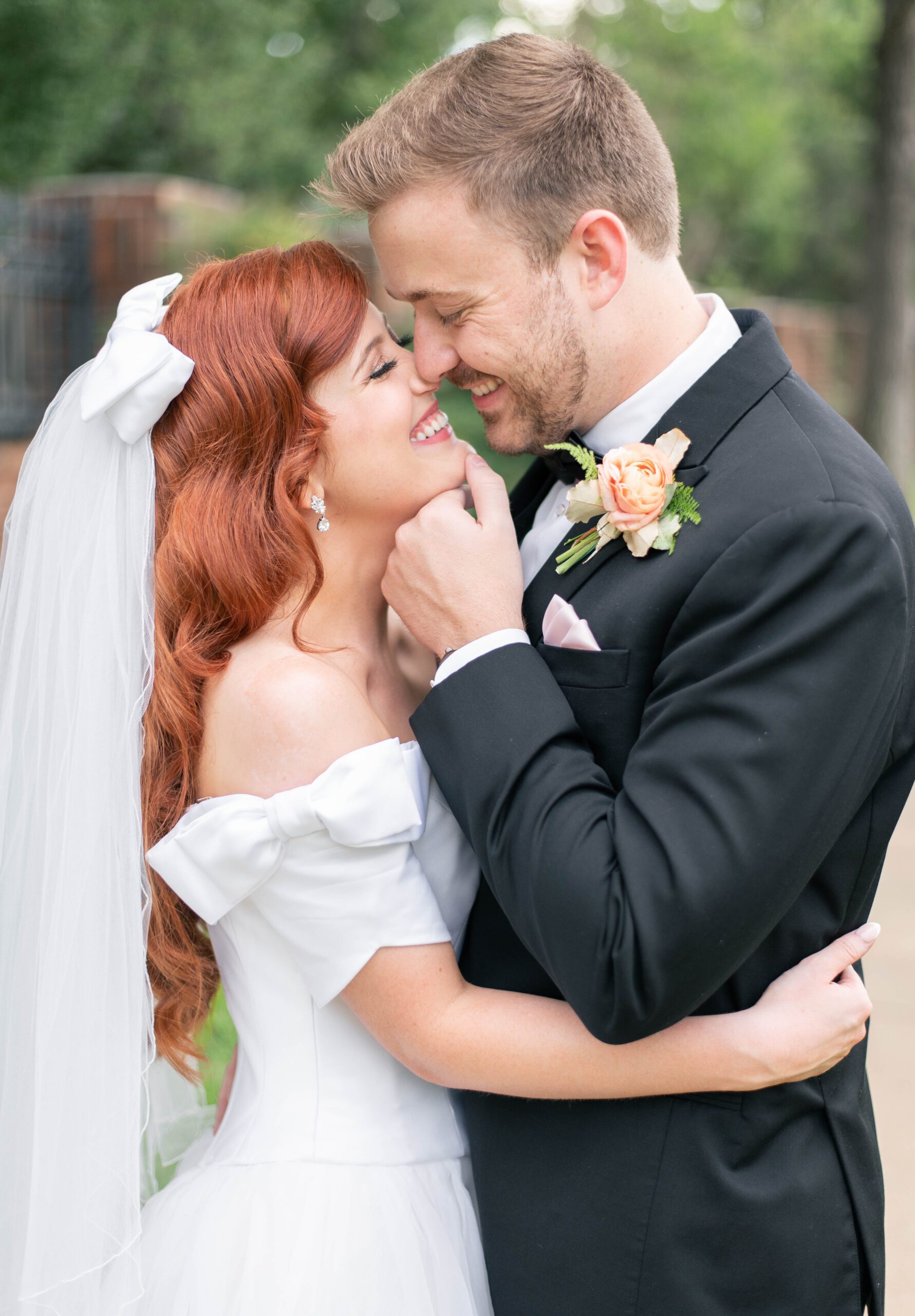bride and groom smile at each other while he gently touches her chin, leaning in for a sweet kiss