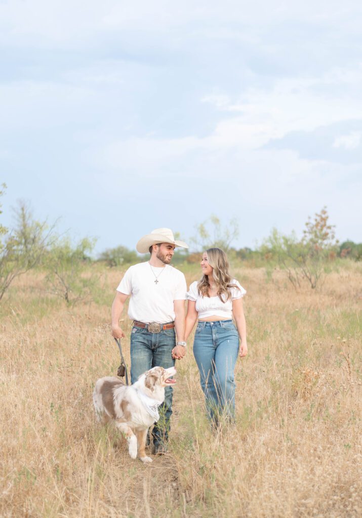 couple walks hand in hand with their Australian Shepard dog through a field at tandy hills in fort worth, Texas