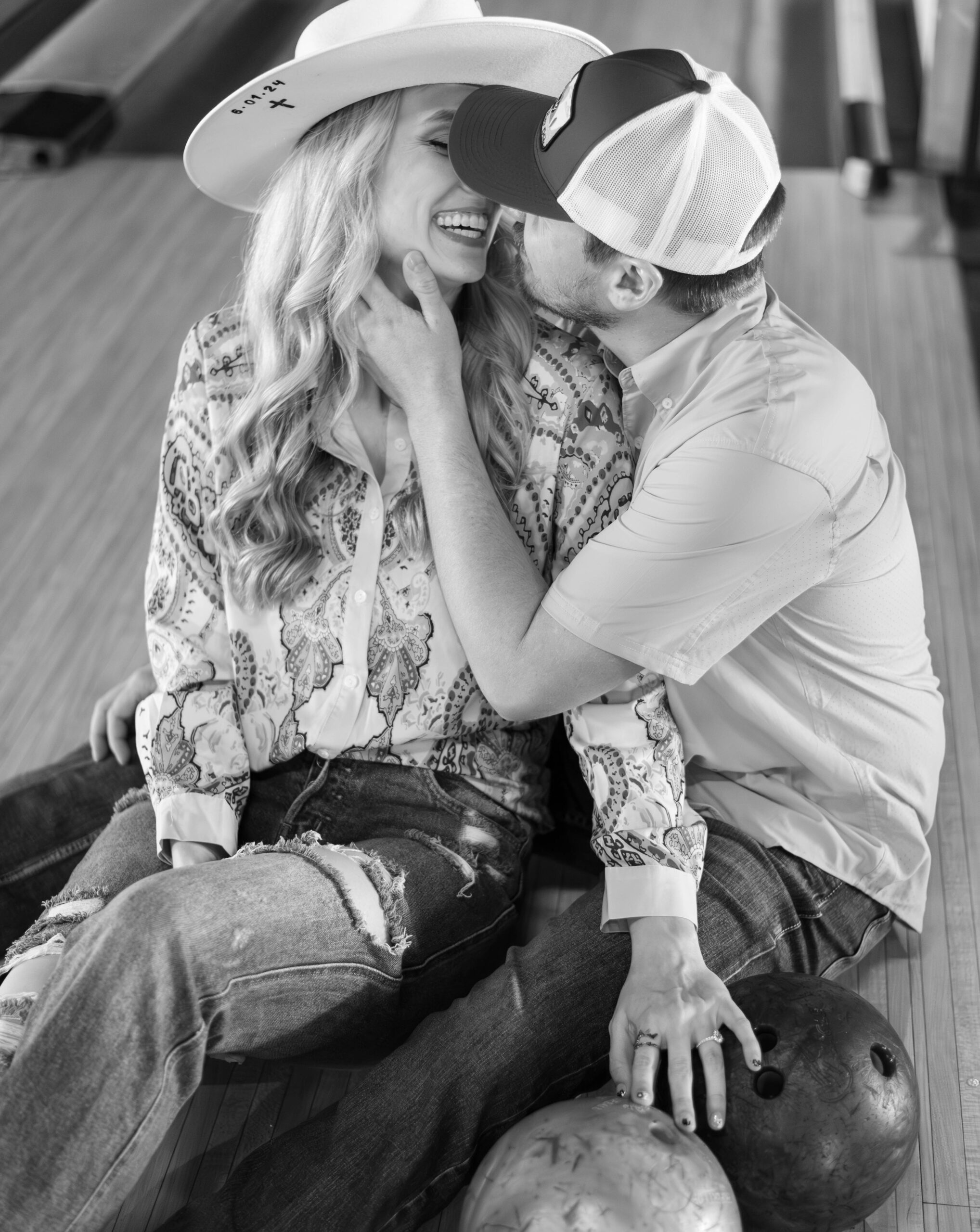 couple laughs while nearly embracing as the man caresses the woman's cheek as they sit on an empty bowling lane at bowlounge dallas